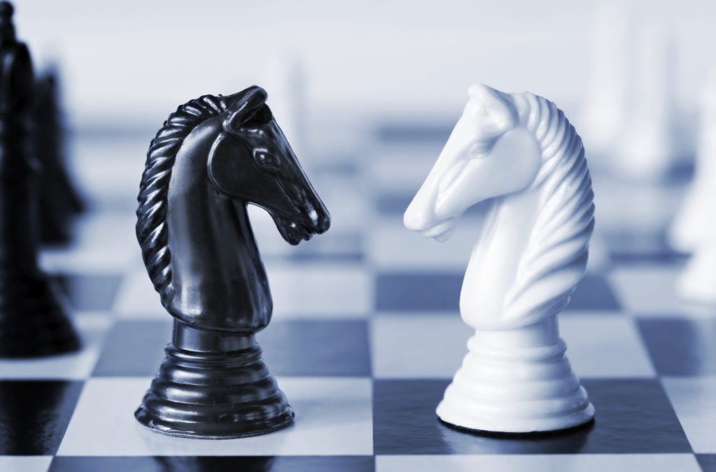 Head to head - knights on a chess board, in blue duotone.  Shallow depth of field.